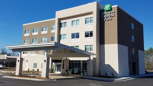 Un bâtiment de la chaîne Holiday Inn Express & Suites, doté d’un design moderne, avec une entrée abritée et de nombreuses fenêtres.