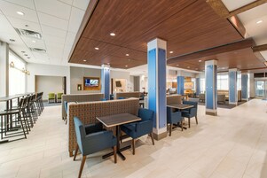 Un restaurante moderno con mesas altas y reservados, techo de madera y vista al salón comedor.