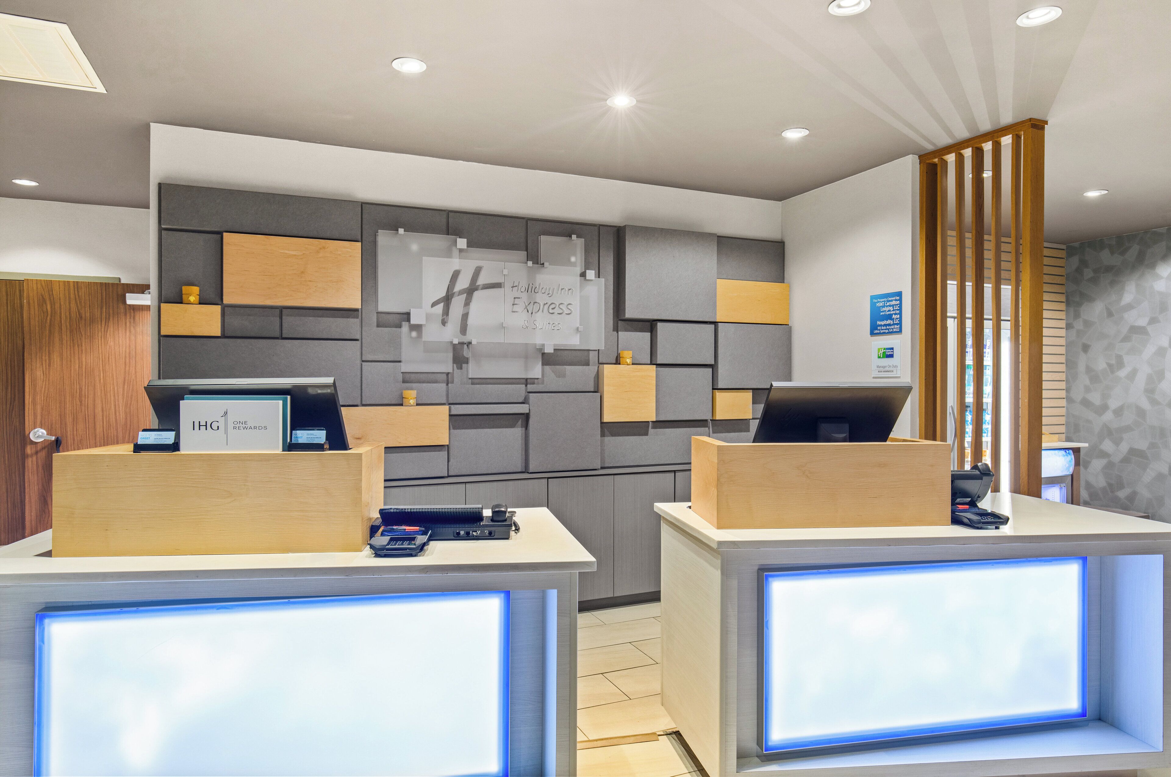 A hotel reception area with a modern design, featuring a reception desk, a digital display, and a sign for 'Holiday Inn Express'.