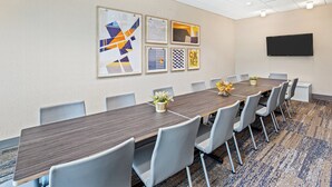Une salle de conférence avec une longue table, des chaises grises et des œuvres d’art encadrées accrochées au mur.