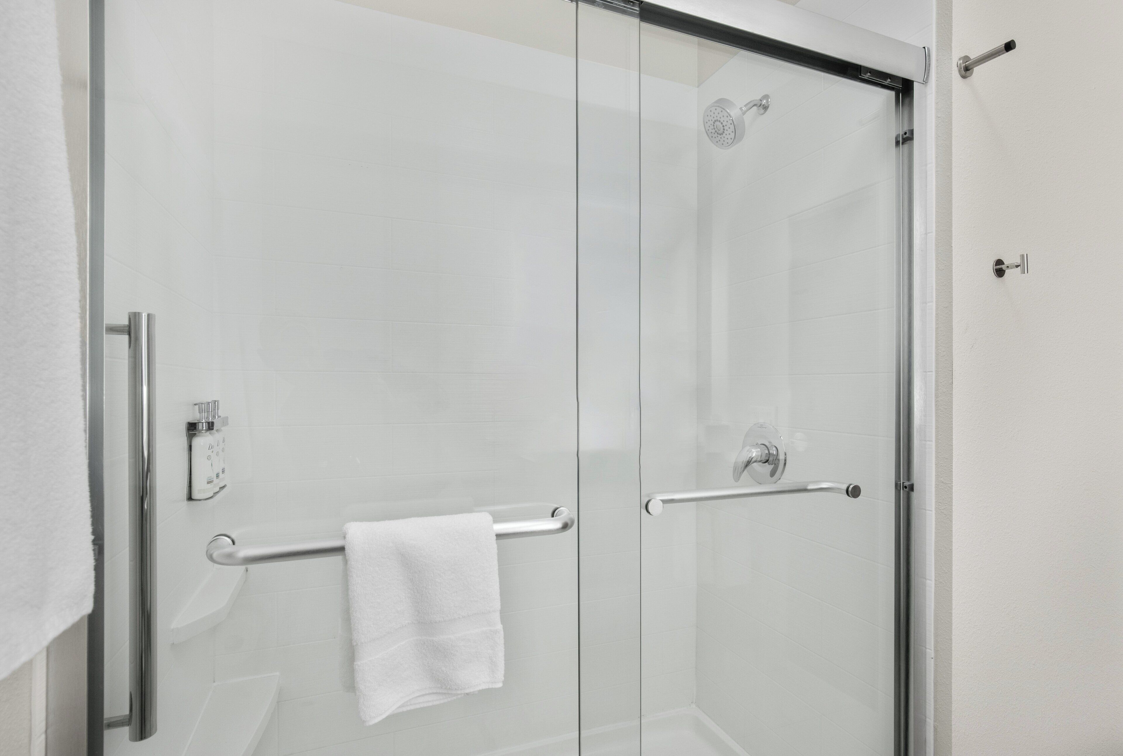 Un bagno moderno con box doccia in vetro, un asciugamano bianco sul porta asciugamani e soffione visibile.