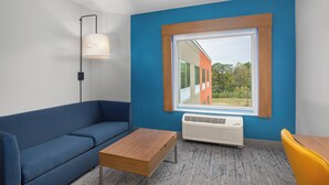 Une pièce moderne avec un mur bleu, une grande fenêtre, un canapé bleu, une table en bois et une chaise jaune.
