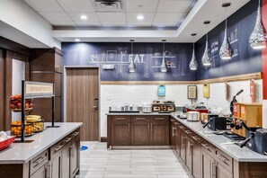 Une cuisine moderne dotée d’un îlot central, de meubles en bois et d’un mur recouvert d’un tableau noir sur lequel sont accrochés des ustensiles de cuisine.