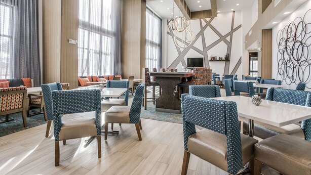 Eine moderne Hotellobby mit Barbereich in der Mitte, Sitzgelegenheiten und einem großen Wandbild.