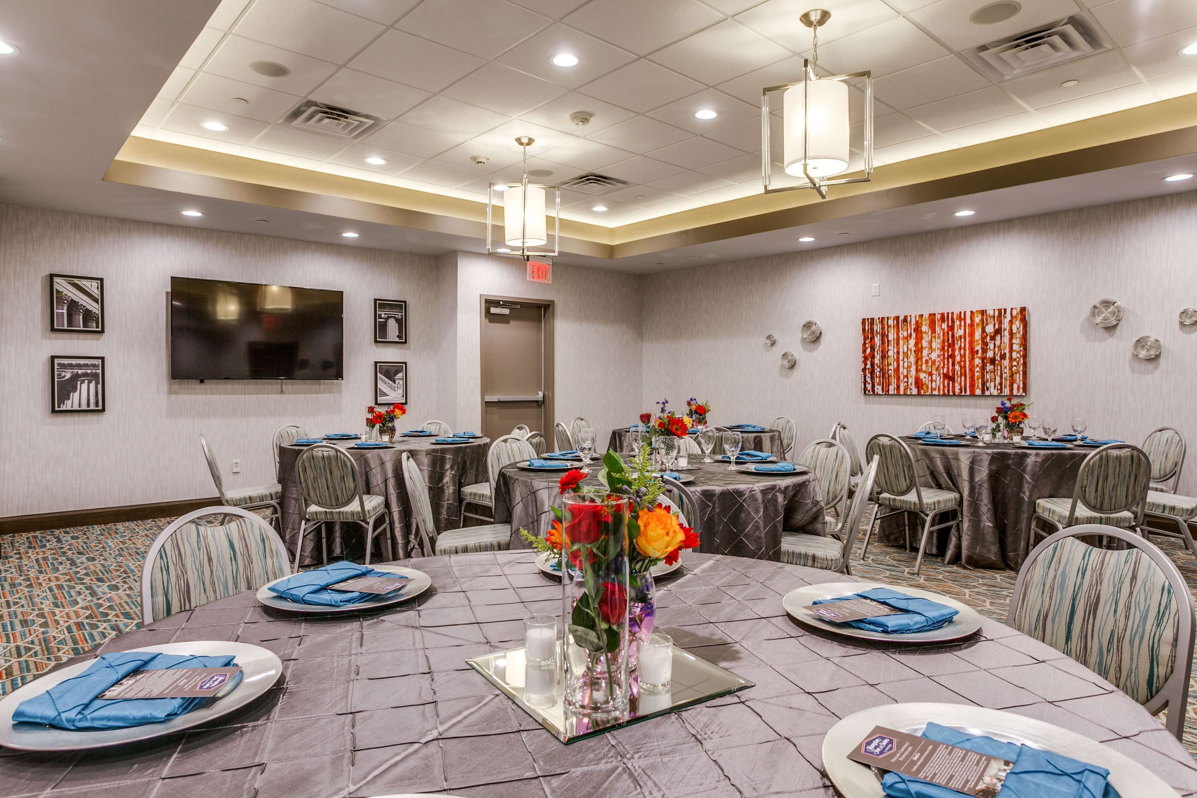 A conference room with round tables, chairs, a large flat-screen TV, and a decorative wall piece.