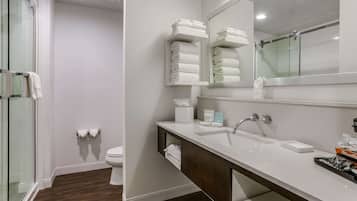 A modern bathroom with a glass shower enclosure, a white toilet, a vanity with a mirror, and neatly stacked towels.