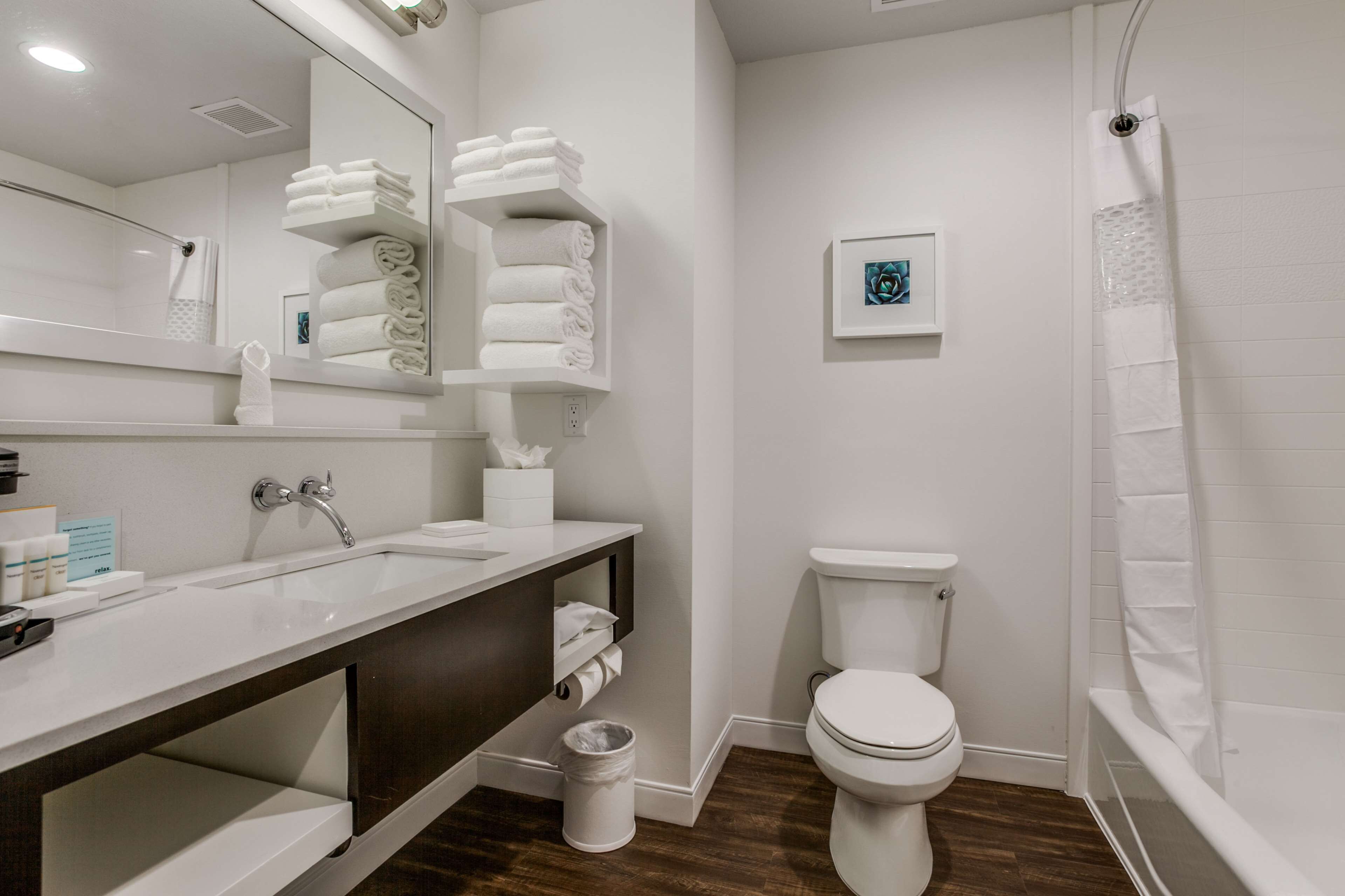 A modern bathroom with a white sink, dark wooden vanity, white toilet, and a shower with a white curtain.