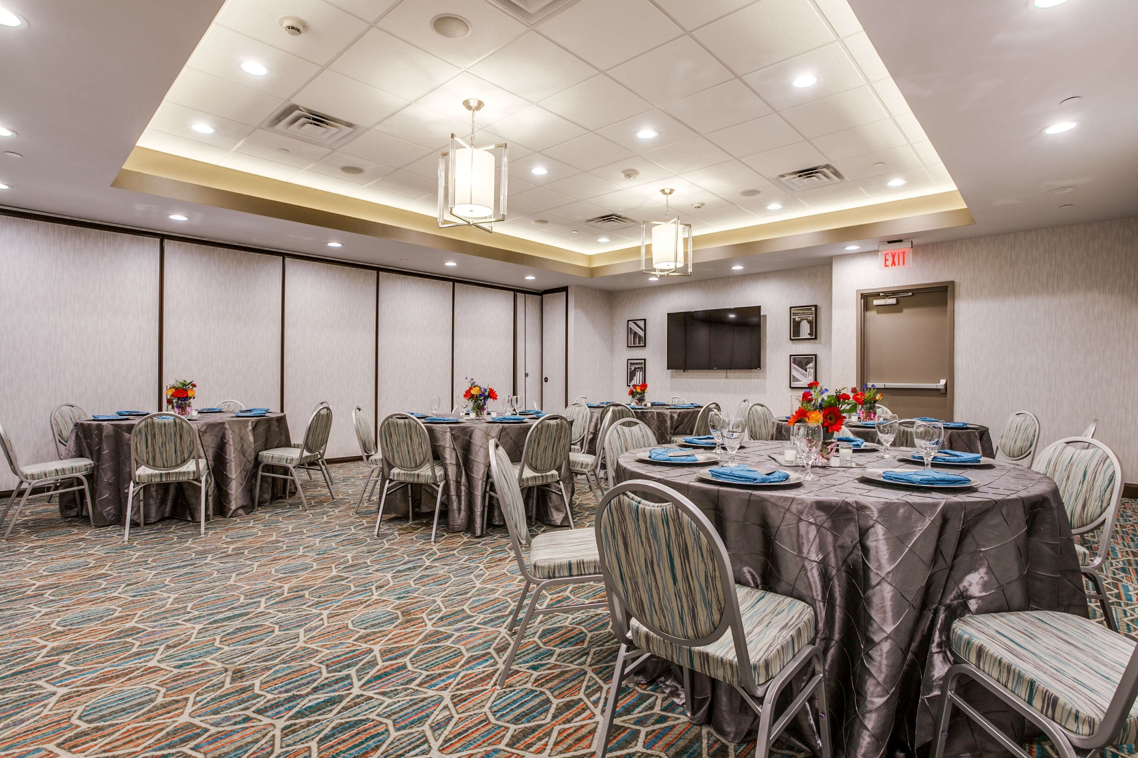 A conference room with multiple tables and chairs, a flat-screen TV, and an exit sign.