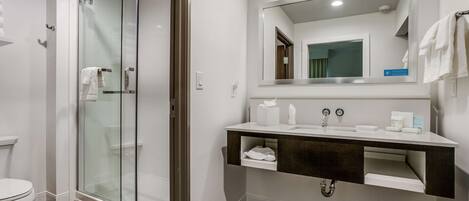 A modern bathroom with a glass-enclosed shower, a white sink with a dark countertop, and a large mirror above the sink.