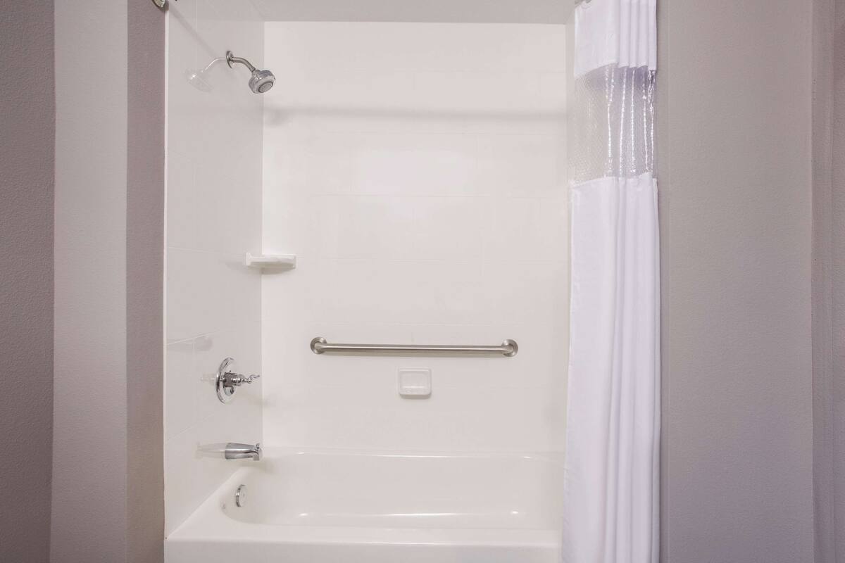 A white bathtub with a handheld showerhead, a grab bar, and a soap dish.