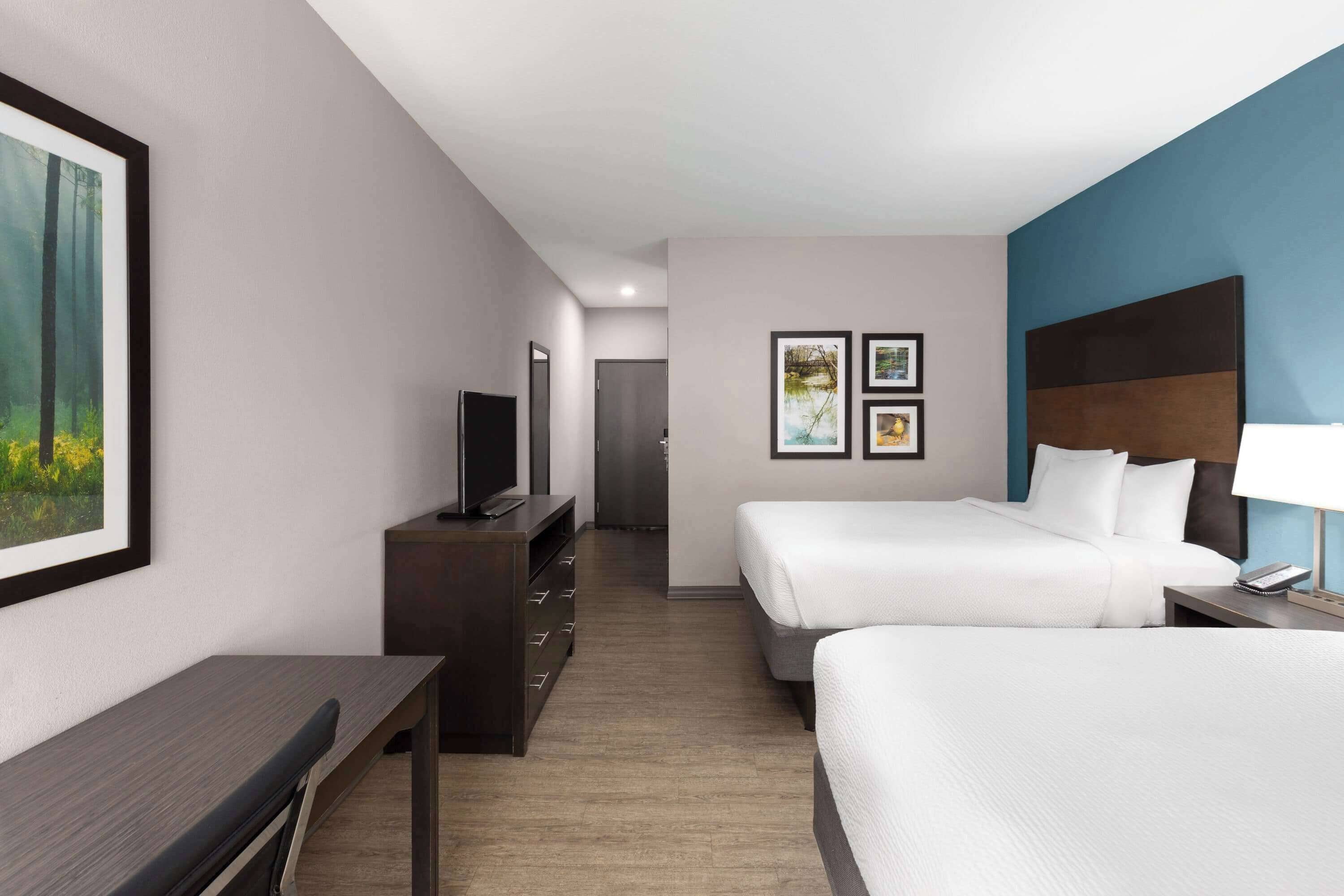 Habitación de hotel con dos camas, un escritorio, un aparador, un televisor y cuadros en la pared.