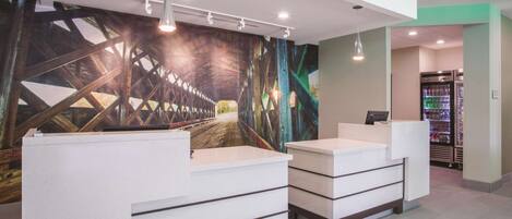 A reception area with two white reception desks, a large mural of a bridge, and a refrigerator in the background.