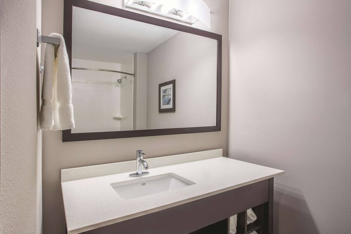 A bathroom with a white sink, a large mirror, and a towel hanging on a rack.