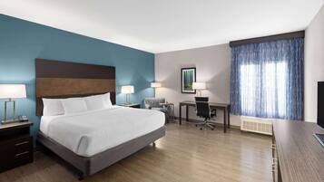 A hotel room with a large bed, two bedside tables with lamps, a desk with a chair, a window with curtains, and a mounted TV.