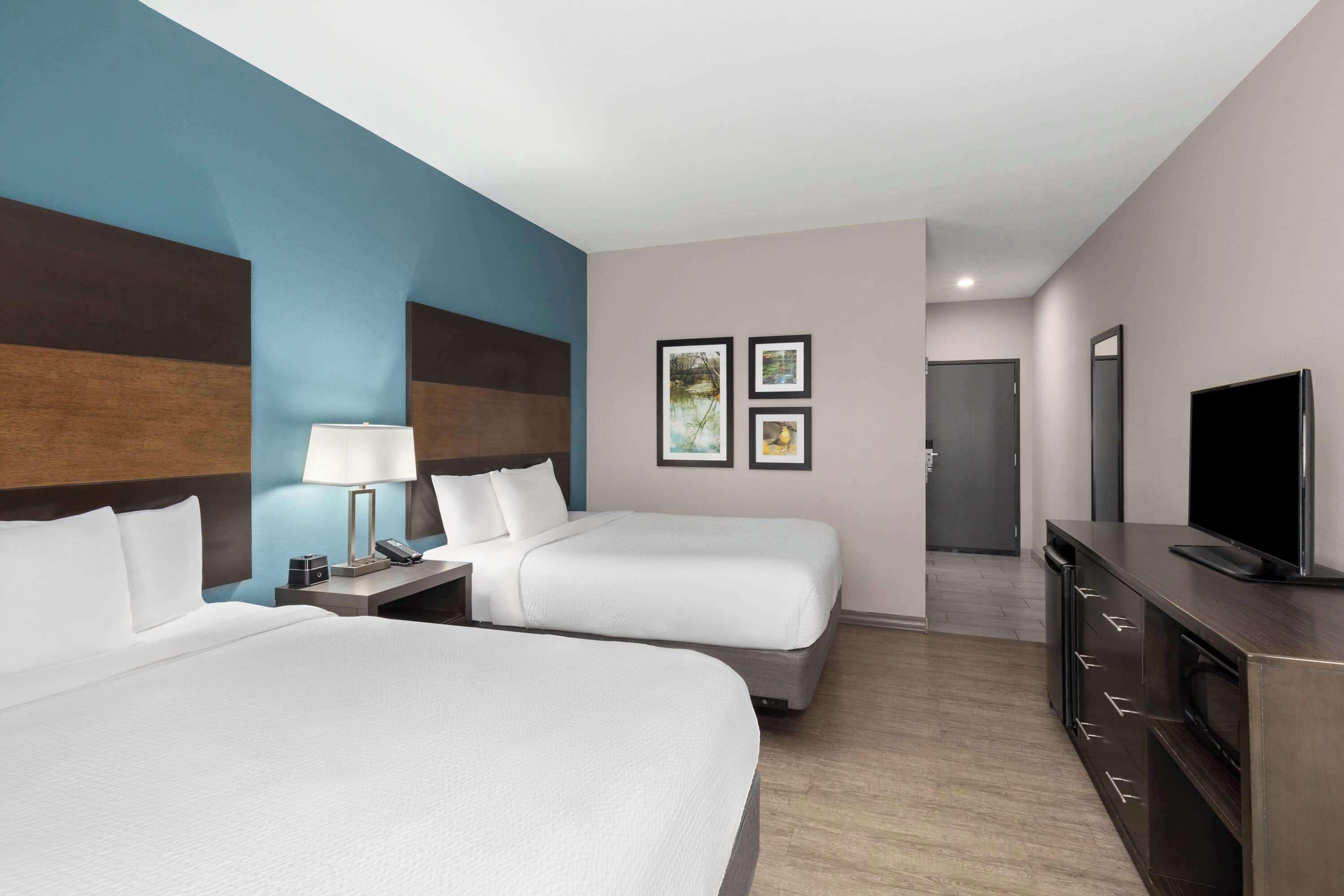A hotel room with two beds, a TV, a dresser, and artwork on the wall.