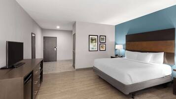 Ein modernes Hotelzimmer mit einem großen Bett, einem Flachbildfernseher, einem Schreibtisch mit Schubladen und einer Tür zu einem weiteren Raum.