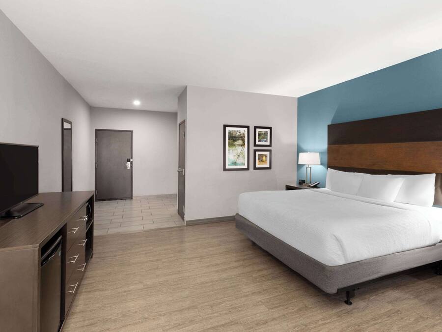 A modern hotel room with a large bed, a flat-screen TV, a desk with drawers, and a door leading to another room.