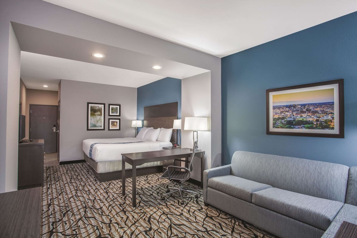 A hotel room with a bed, a desk, a chair, a sofa, and a framed cityscape picture on the wall.