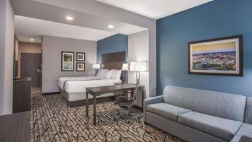 A hotel room with a bed, a desk, a chair, a sofa, and a framed cityscape picture on the wall.