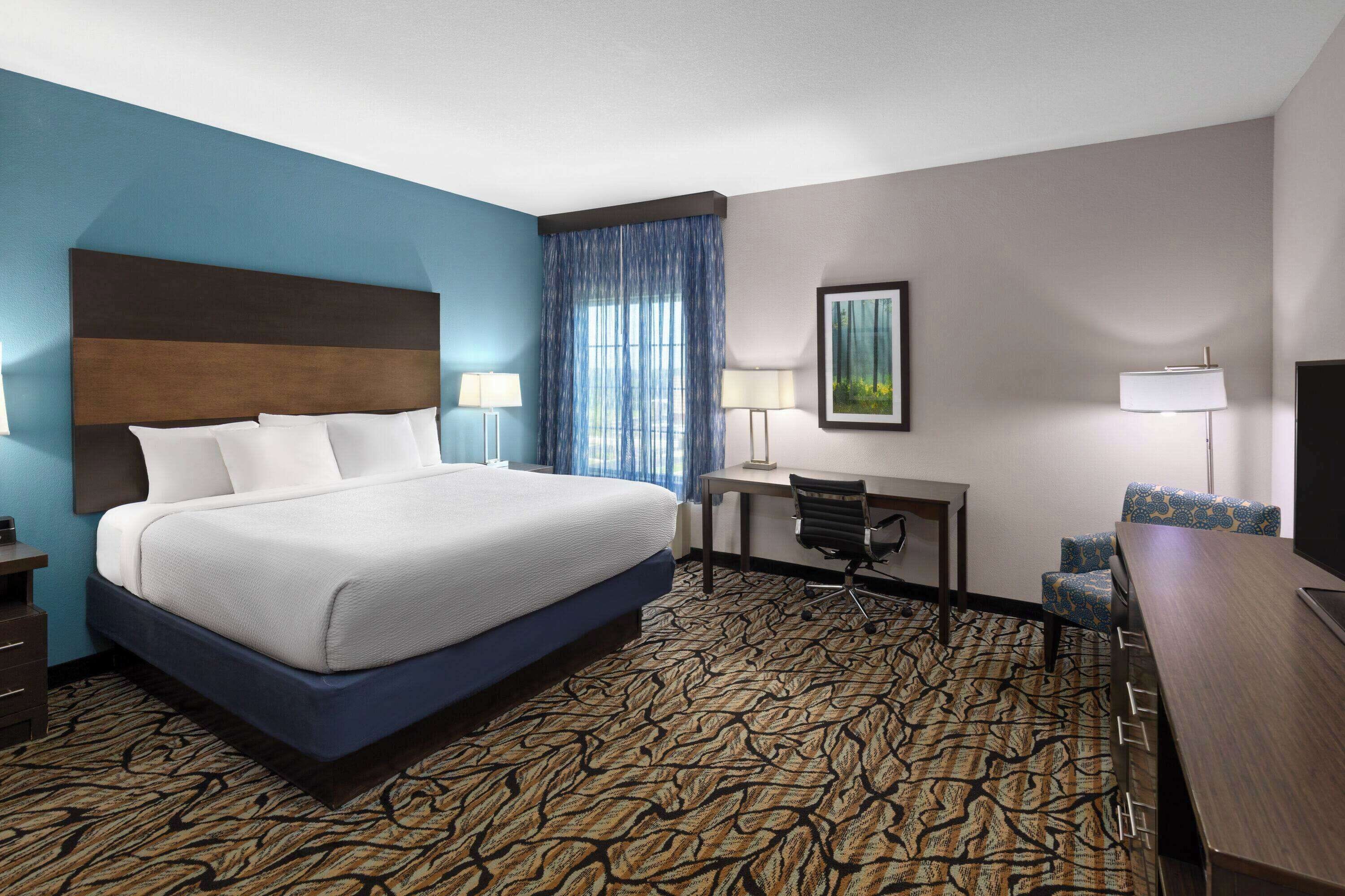 A hotel room with a large bed, a desk, two chairs, and a patterned carpet.