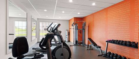 Une salle de sport équipée de matériel d’exercice, un mur orné de citations motivantes et une fenêtre donnant sur un paysage verdoyant.