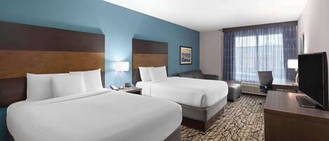 A hotel room with two beds, a desk, a chair, a TV, and a window with curtains.