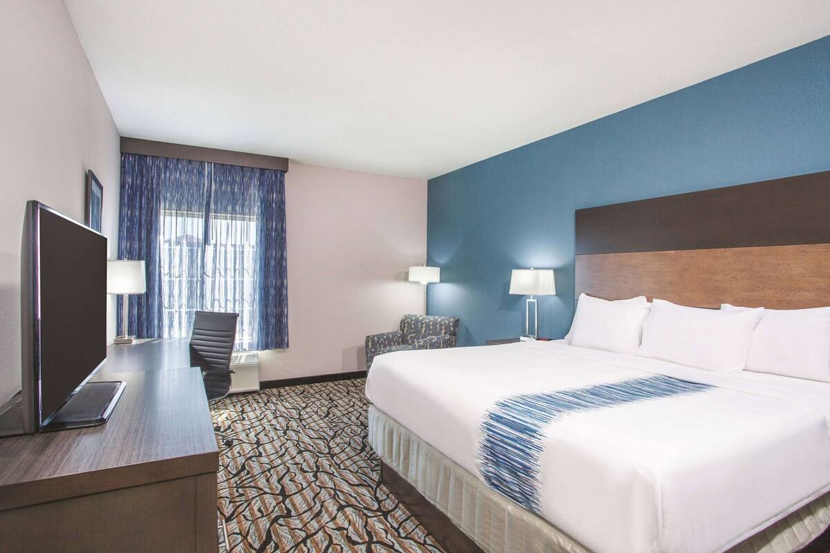 A hotel room with a bed, a desk with a TV, a chair, a lamp, and a window with curtains.