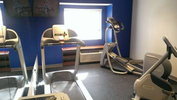 Un gimnasio con cintas de correr, elípticas y una banca.