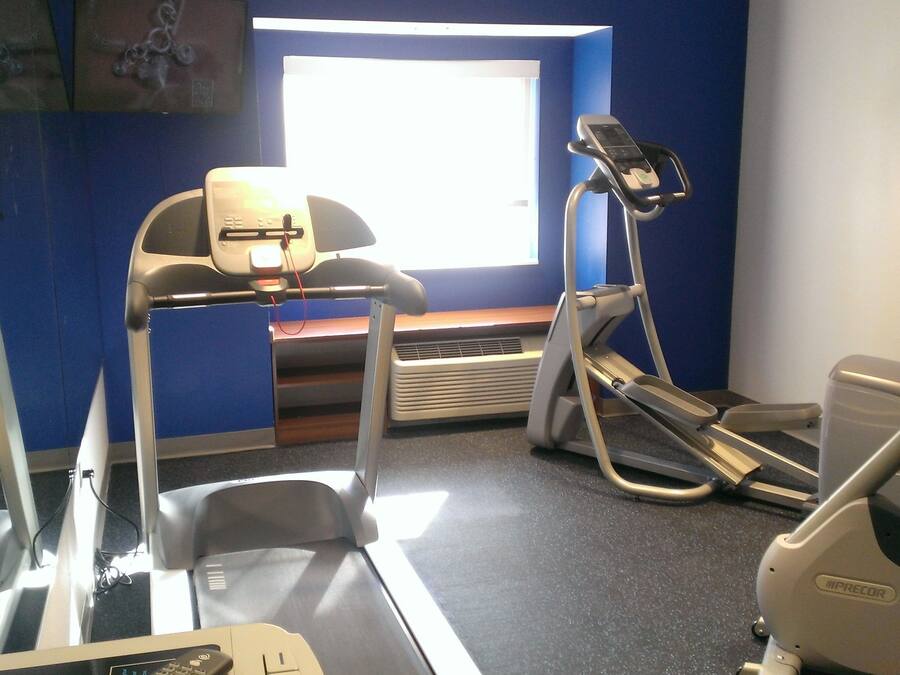 Un gimnasio con cintas de correr, elípticas y una banca.