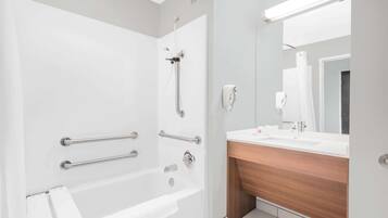 Ein modernes Badezimmer mit barrierefreier Dusche, Haltegriffen, einem weißen Waschbecken und einem großen Spiegel.