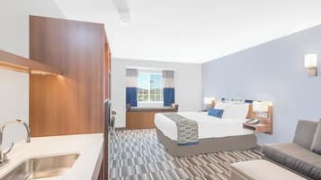 Una camera d'albergo con un letto, una poltrona, una scrivania, una lampada, un telefono e una finestra con tende.