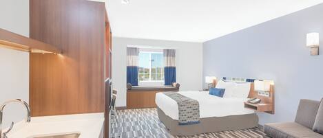 Habitación de hotel con cama, sofá, escritorio, lámpara, teléfono y ventana con cortinas.