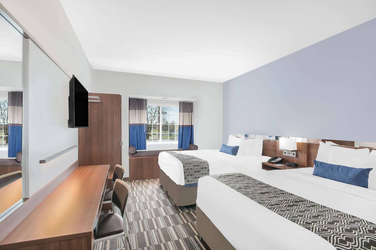 A hotel room with a bed, a desk, a chair, a TV, and a window with curtains.