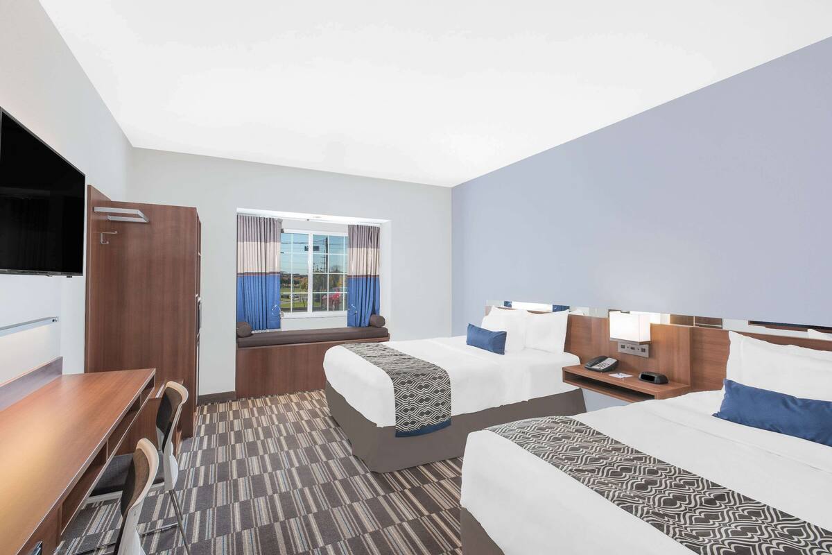 A hotel room with two beds, a desk, and a TV.