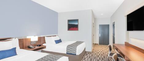 Habitación de hotel con dos camas, un escritorio, una silla, un televisor de pantalla plana y un cuadro en la pared.
