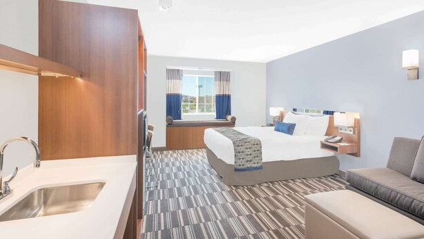 A hotel room with a bed, a sofa, a desk, and a window with curtains. - Microtel Inn & Suites By Wyndham Binghamton (Binghamton)