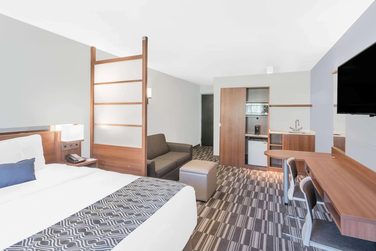 A hotel room with a bed, a desk, a kitchenette, and a TV.
