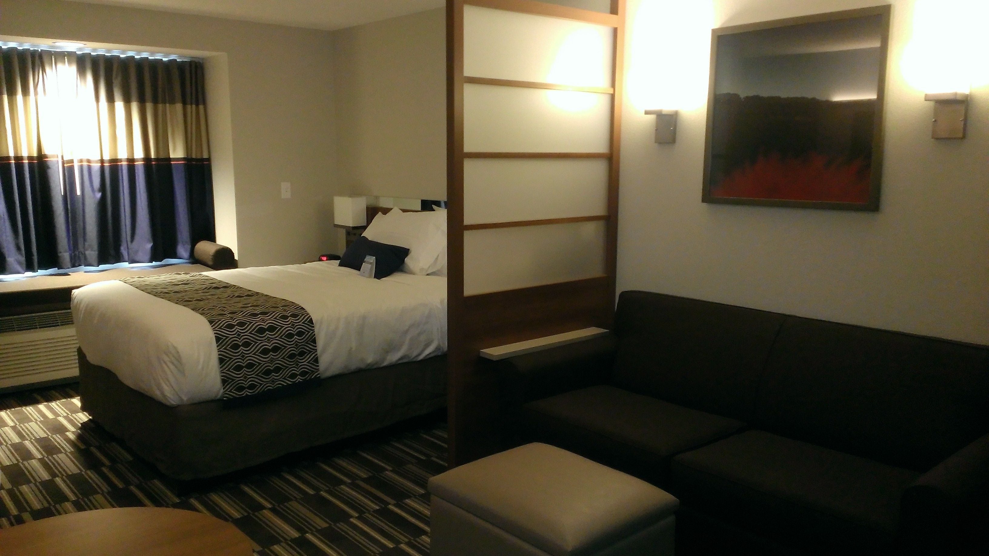 A hotel room with a bed, a sofa, a small table, and a window with curtains.