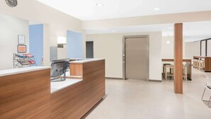 A reception area with a wooden reception desk, a clock, and a wall-mounted sign. - Microtel Inn & Suites By Wyndham Binghamton (Binghamton)