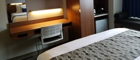 Une chambre d’hôtel comprenant un lit, un bureau avec une chaise, un téléviseur fixé au-dessus du bureau, un four à micro-ondes et une machine à café.