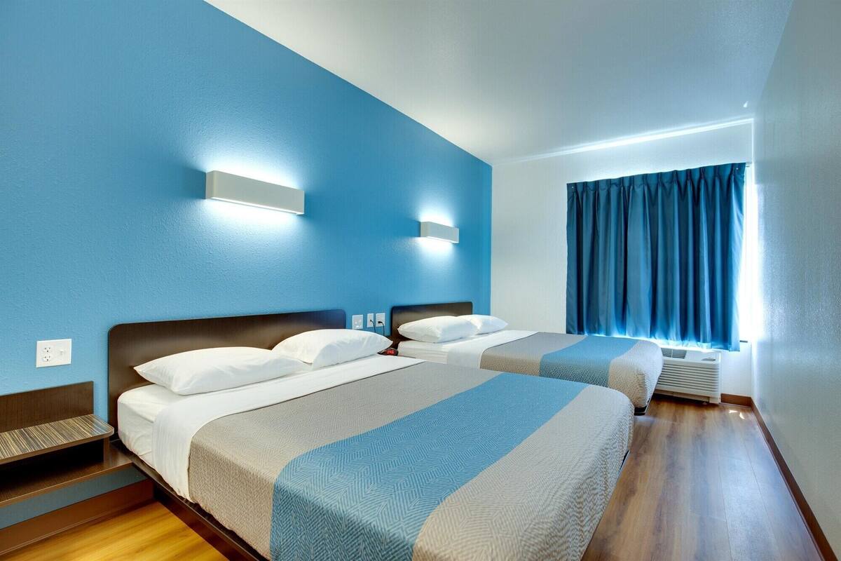 Habitación de hotel con dos camas, un ventanal con cortinas y un equipo de aire acondicionado integrado.
