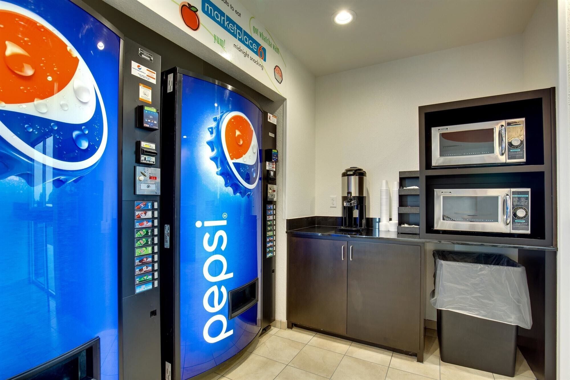 Una cuina compacta amb microones, cafetera i màquina expenedora de Pepsi.