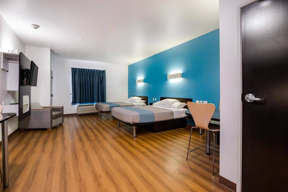 Una habitación de hotel con dos camas, un escritorio, una silla, un televisor y una puerta oscura.