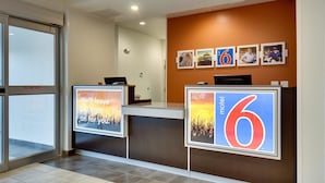 A hotel reception area with a modern design, featuring a reception desk, a glass door, and a wall with framed pictures and a large number '6' sign. - Motel 6 Poplar Bluff, MO (Poplar Bluff)