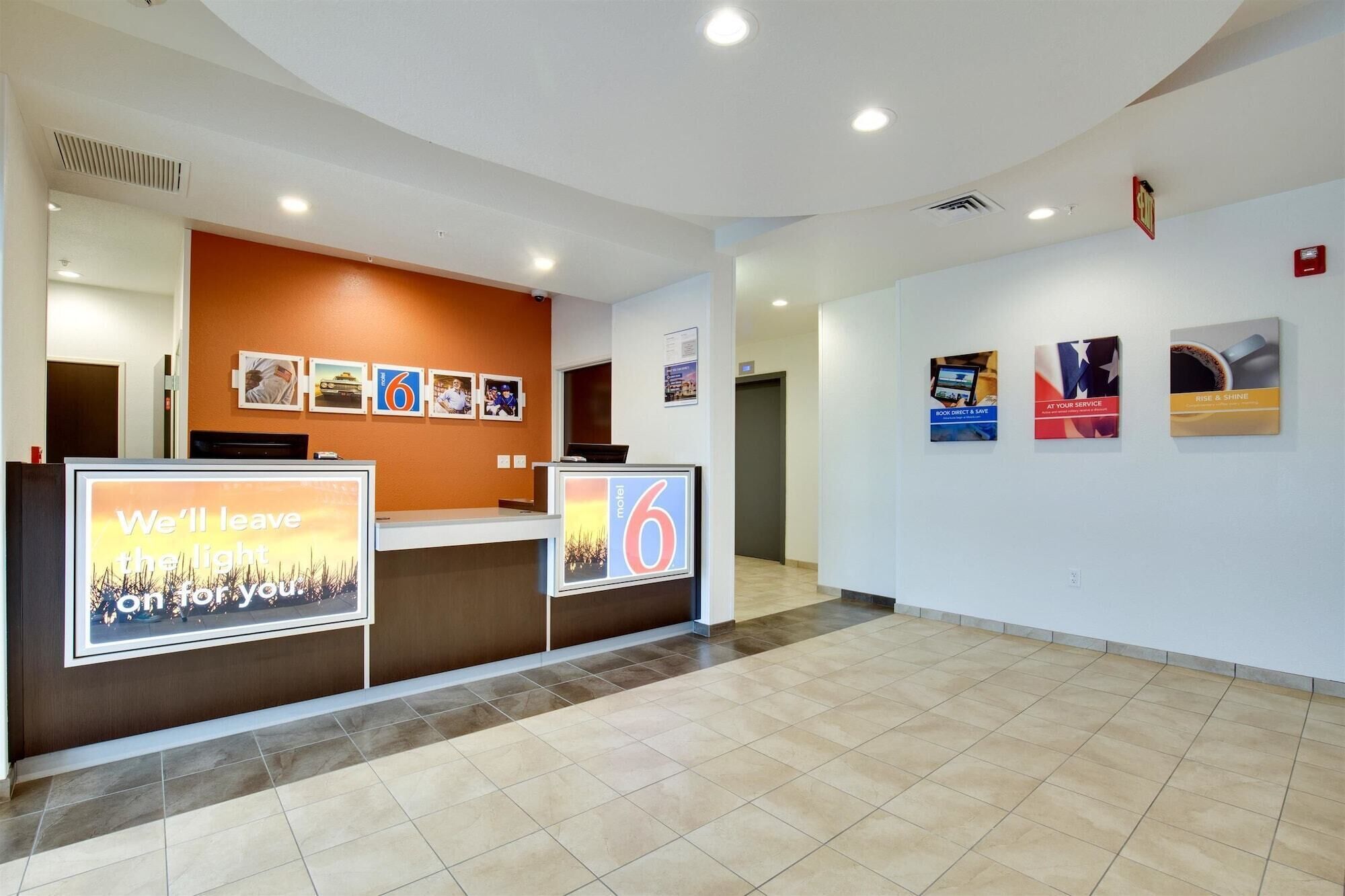 Un espace d’accueil d’hôtel au design moderne, comprenant un comptoir d’accueil, un mur où sont exposées des photos et un sol carrelé, propre et élégant.