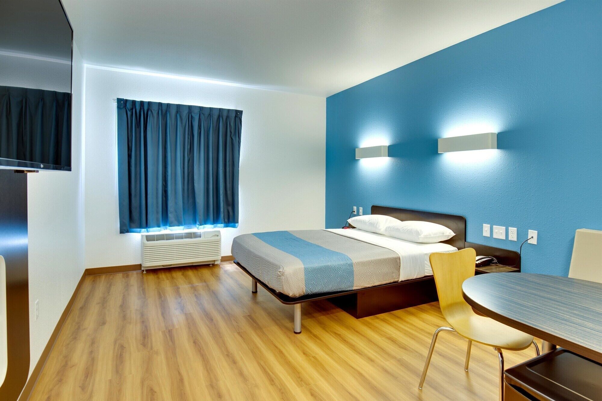 Une chambre d’hôtel moderne équipée d’un lit, d’une table de chevet, d’une chaise et d’un téléviseur à écran plat.