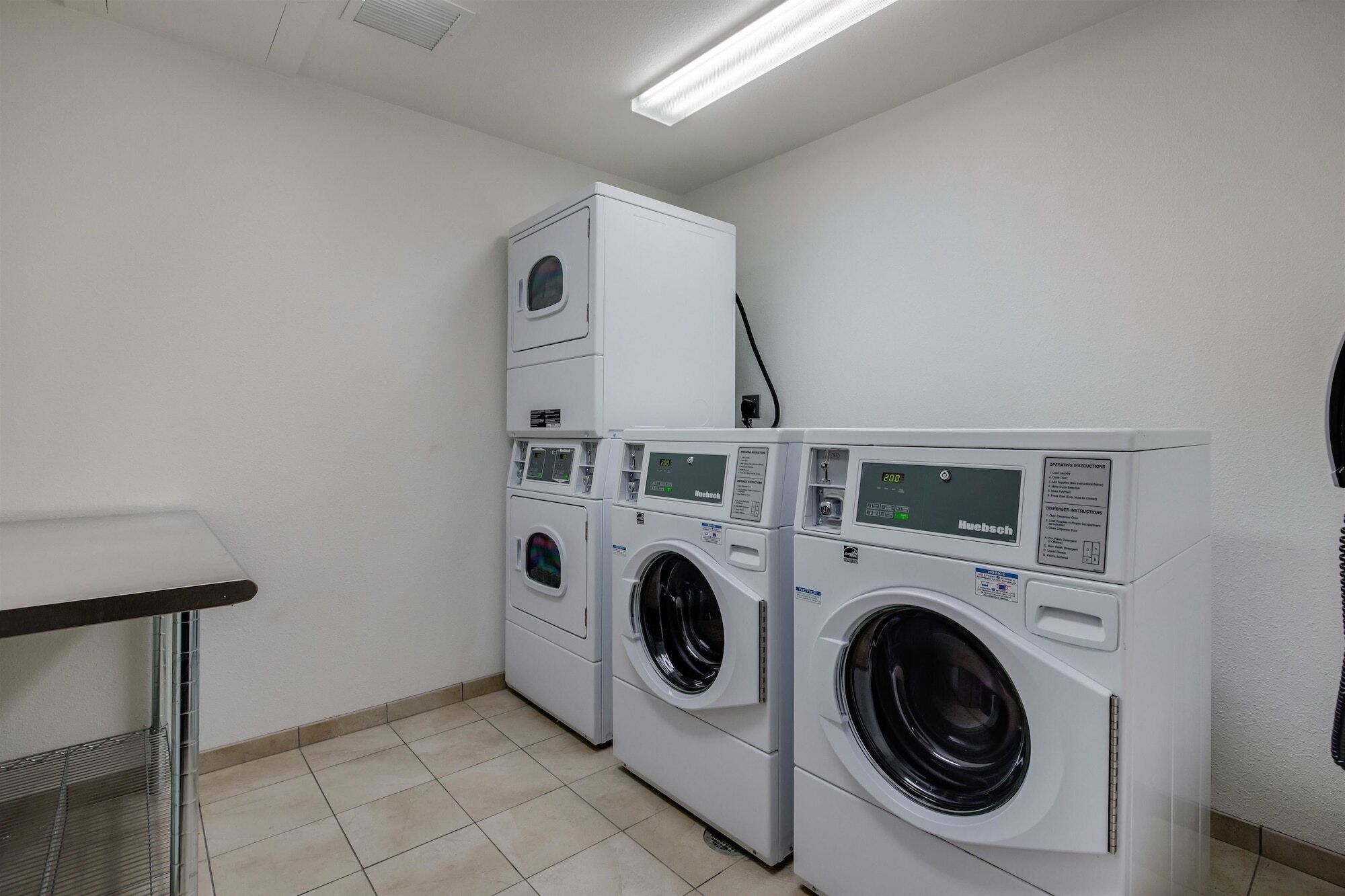 A laundry room with two front-loading washing machines and a stacked dryer.