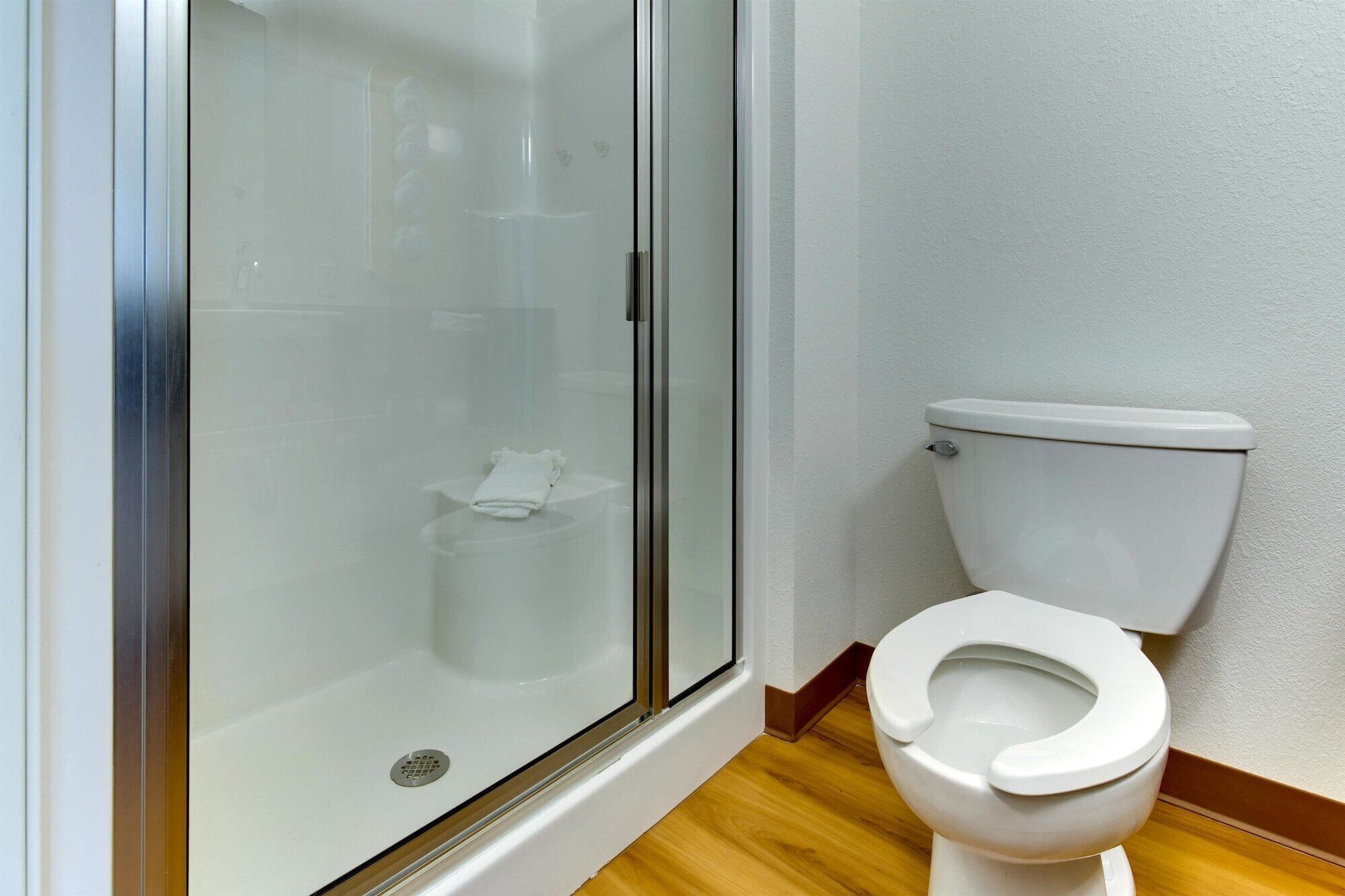 Ein Badezimmer mit Duschkabine aus Glas, Toilette und Holzboden.