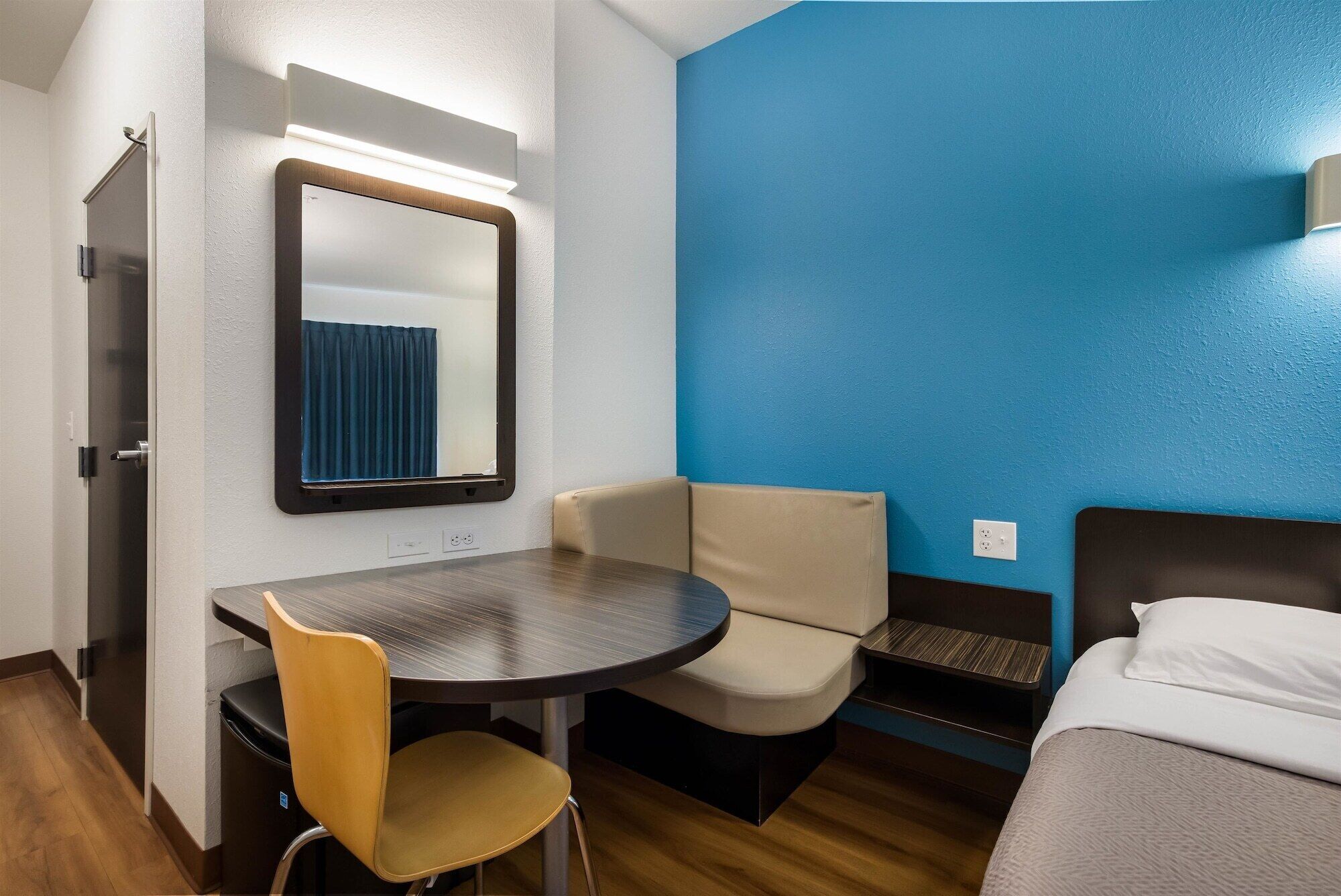 Une chambre d’hôtel compacte comprenant une table ronde, une chaise, un lit et un mur d’accent bleu.