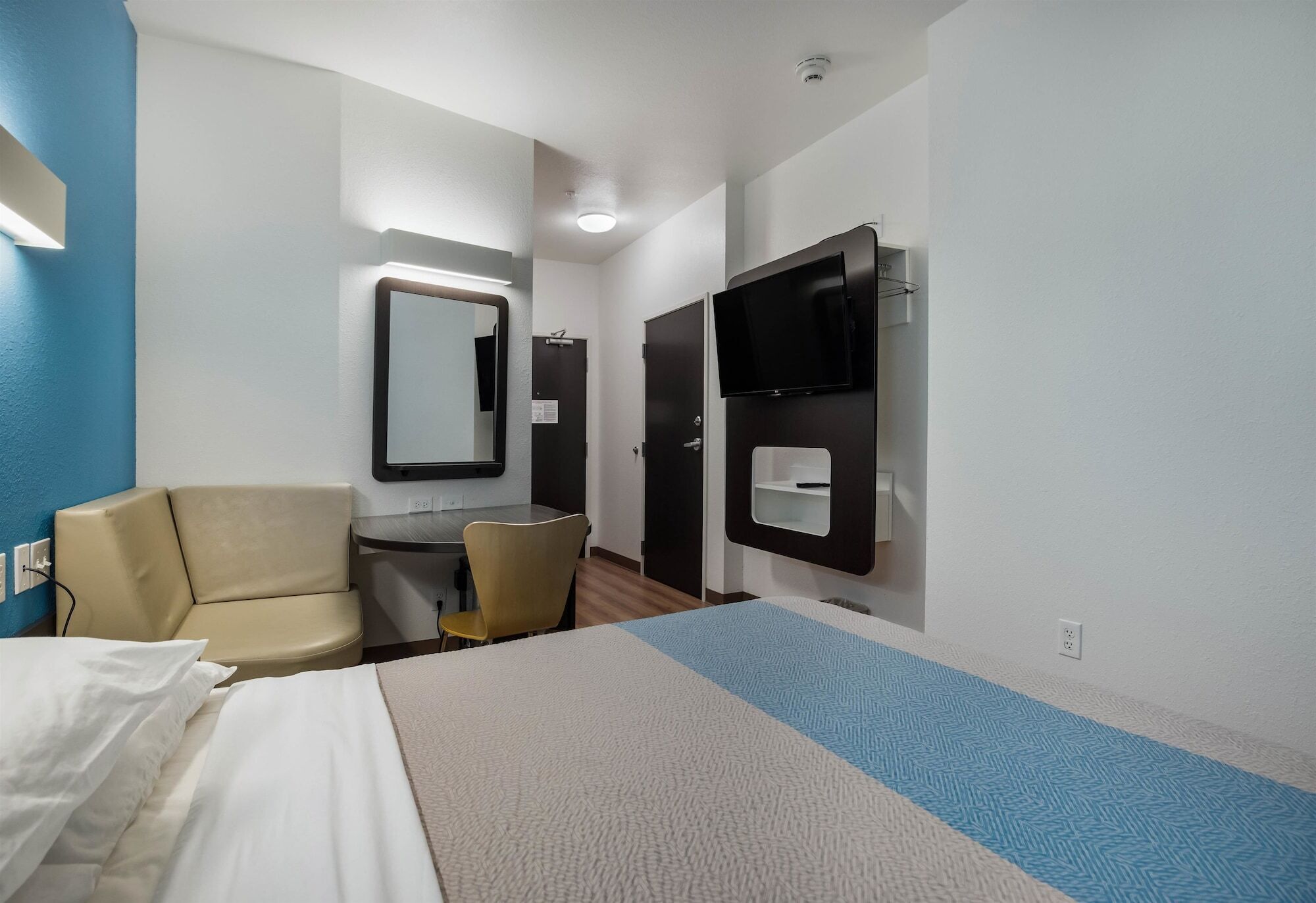 A hotel room with a bed, a desk, a chair, a television, and a mirror.